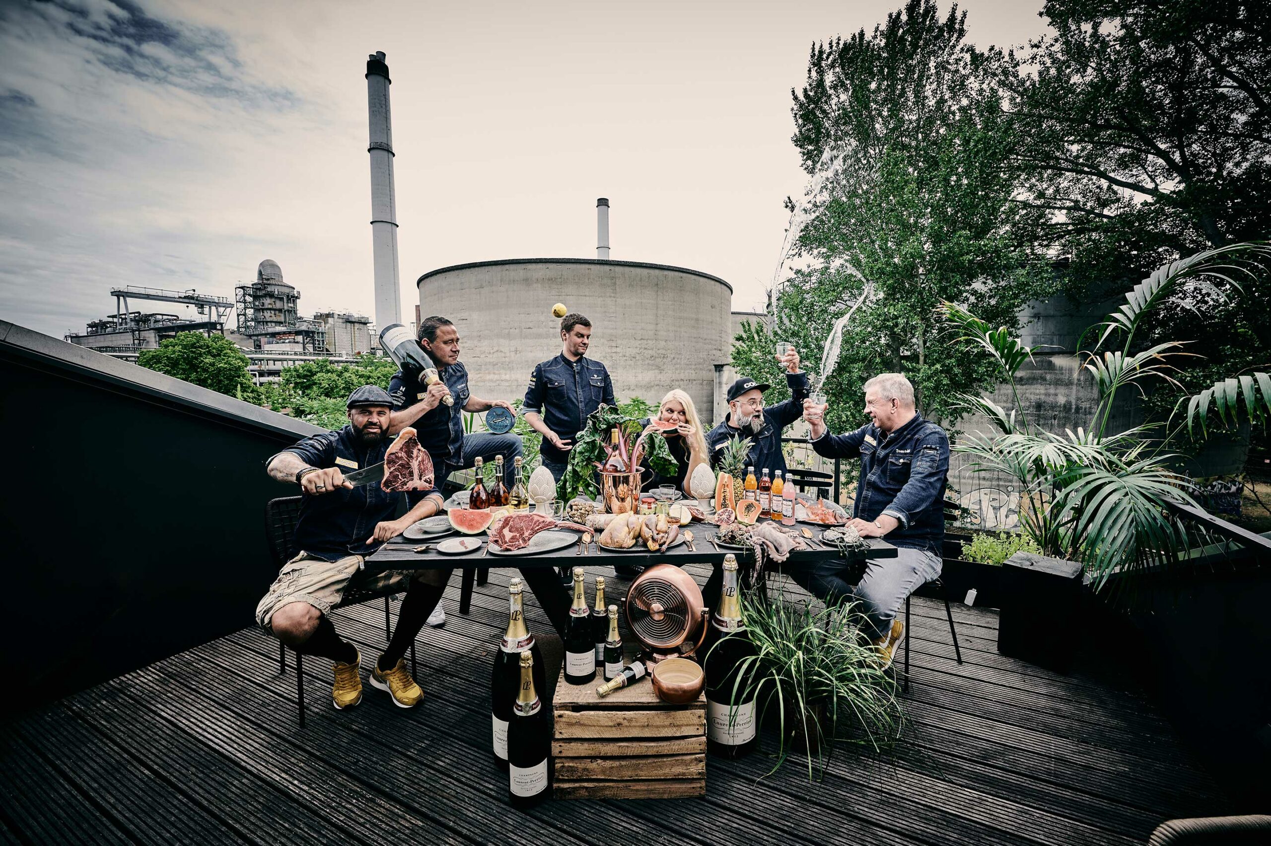Sechs Personen sitzen um einen gedeckten Tisch auf einer Terrasse