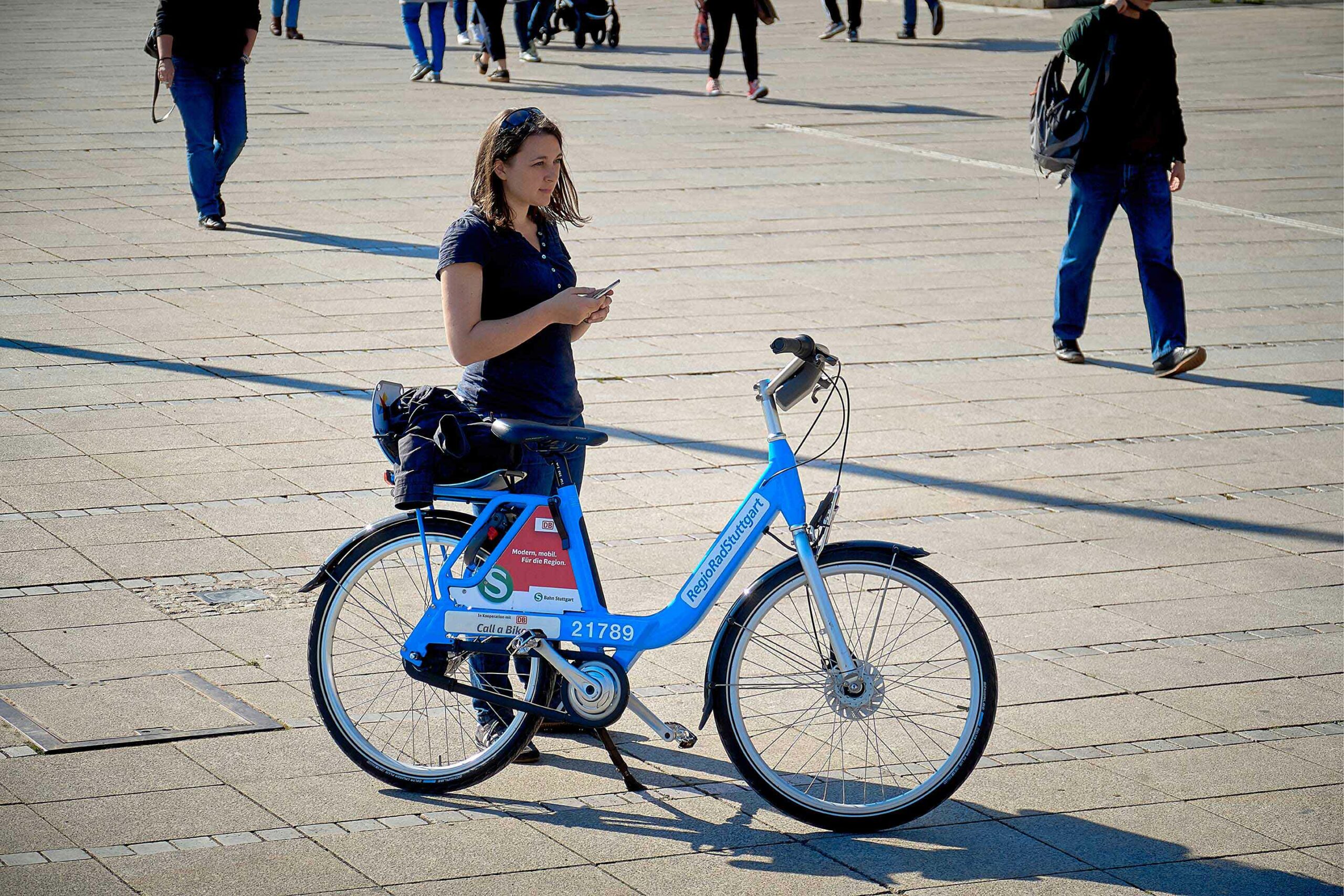 Frau mit Handy in der Hand, blaues Fahrrad steht vor ihr, RegioRad Stuttgart
