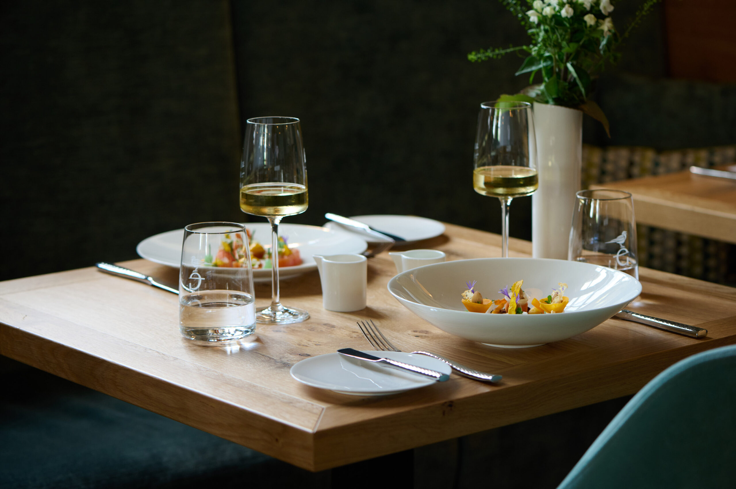 Speise in rundem, weißen, tiefen Teller mit Weißwein in einem Glas. Im Hintergrund steht eine Blume.